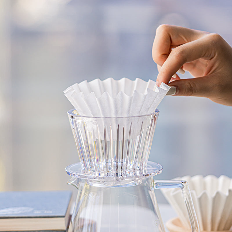 Hand placing a clear plastic coffee filter into the transparent Timemore B75 Crystal Eye Flat Bottom Dripper/Brewer