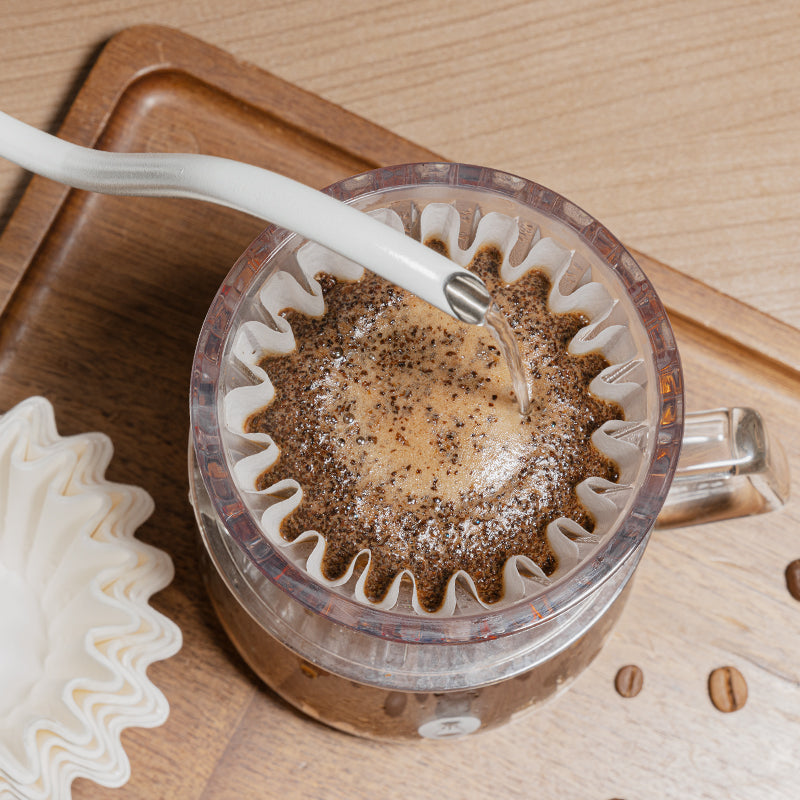 Coffee filter with coffee grounds being poured into it on a wooden surface
