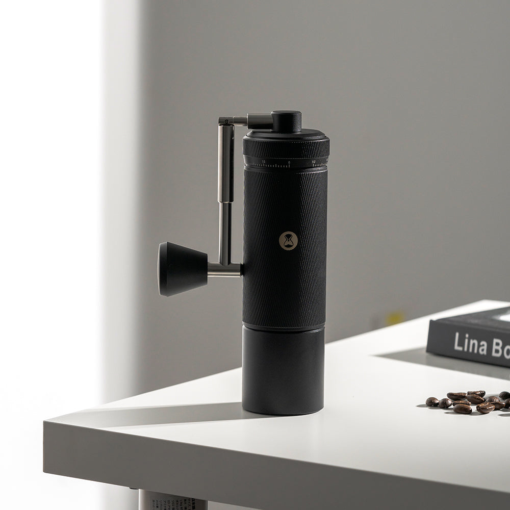 Black Timemore S3 Chestnut Manual Grinder on a white surface with coffee beans nearby